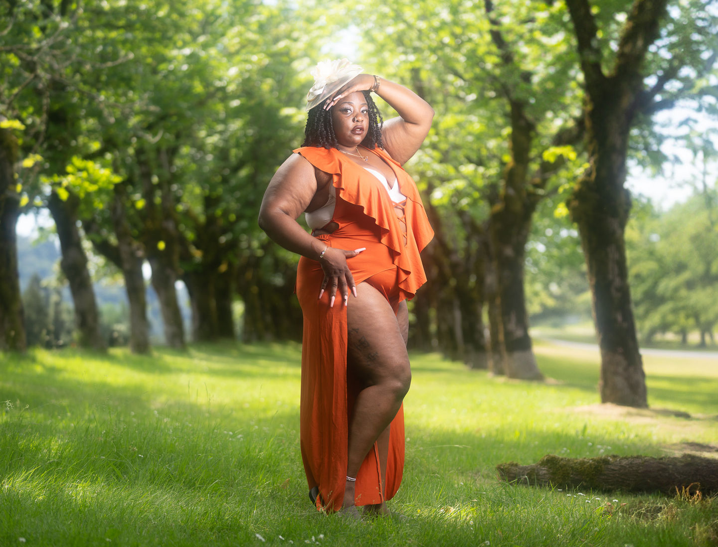 Woman in orange dress posing in sunlit forest.