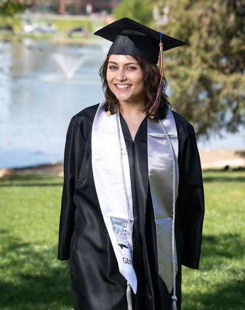 Graduate in cap and gown smiling outdoors.