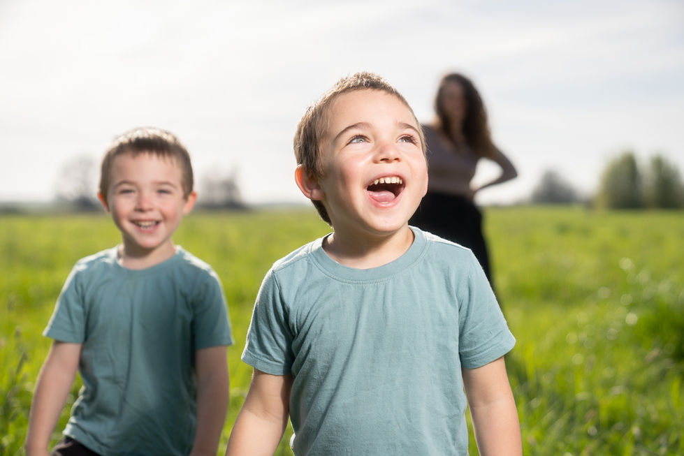Two smiling children outdoors, woman in background.