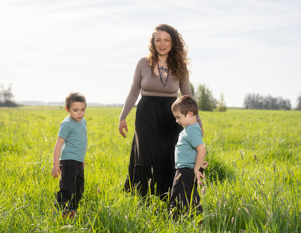 Woman and two children standing in grassy field.