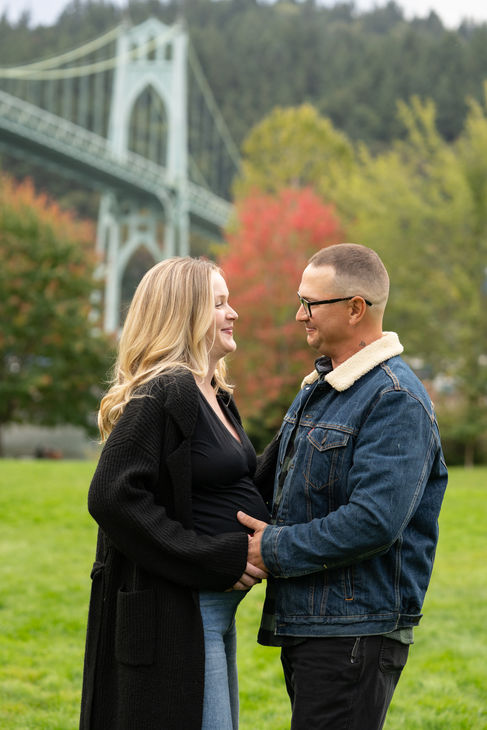 Couple smiling in park with bridge in background.