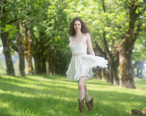 Woman in white dress and boots, standing in park.