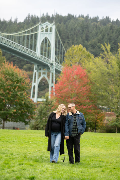 Couple walking in park near a bridge.