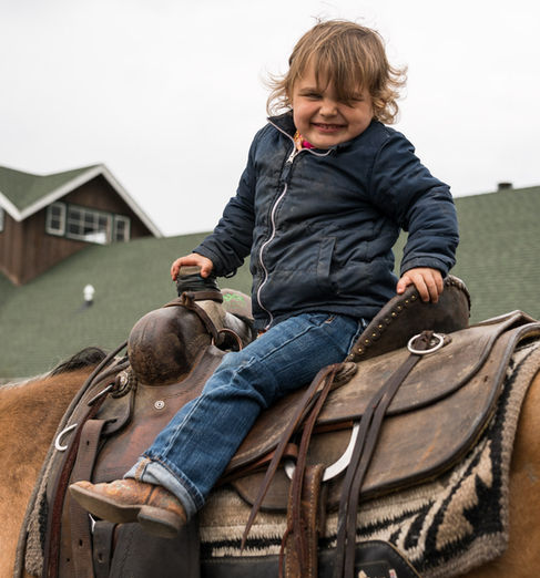 Child smiling while sitting on a saddled horse.