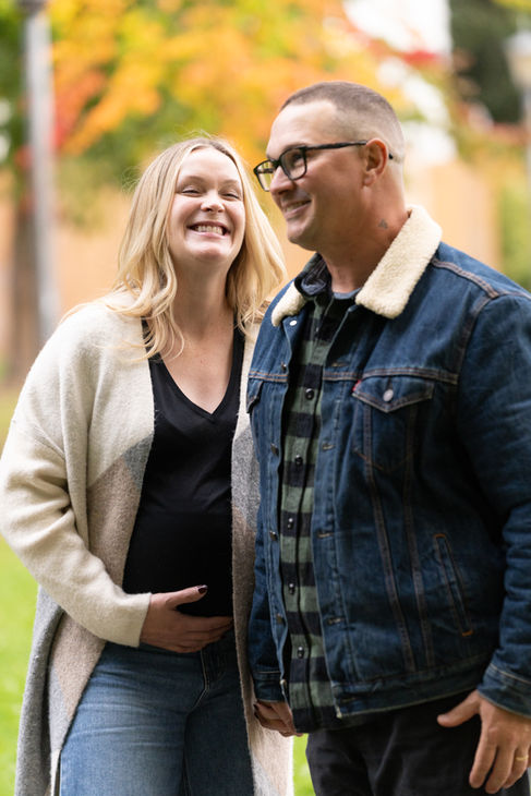 Smiling couple outdoors, woman touching her belly.