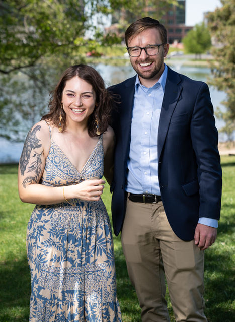 A smiling couple posing outdoors by a lake.