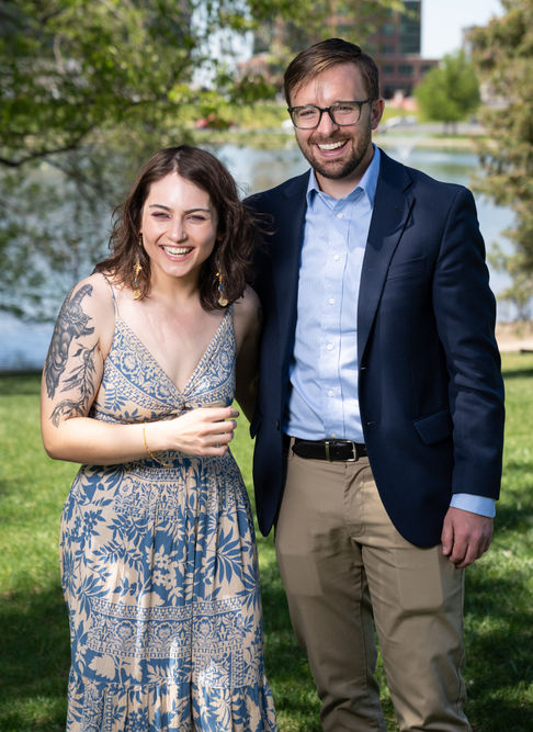 A smiling couple posing outdoors by a lake.