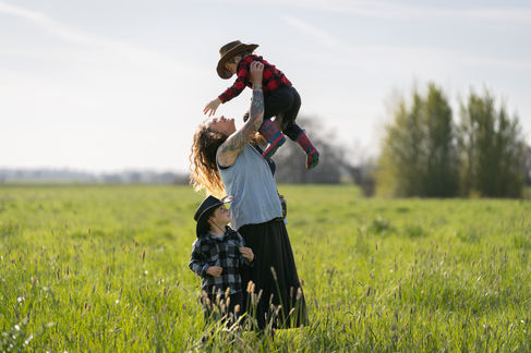 Mother lifting child in a grassy field.