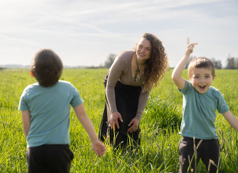 Woman and two children playing in a grassy field.