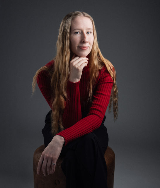 Person sitting, wearing red sweater, long hair, neutral background.