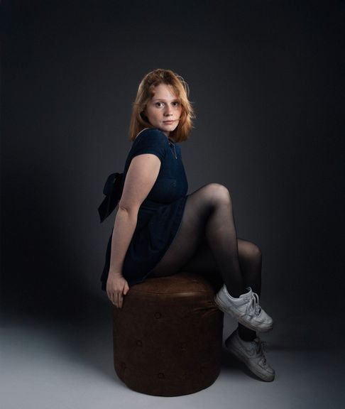 Person sitting on a stool in a dark setting.