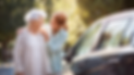 Foto de duas mulheres sorrindo para si com carro ao lado em dia ensolarado