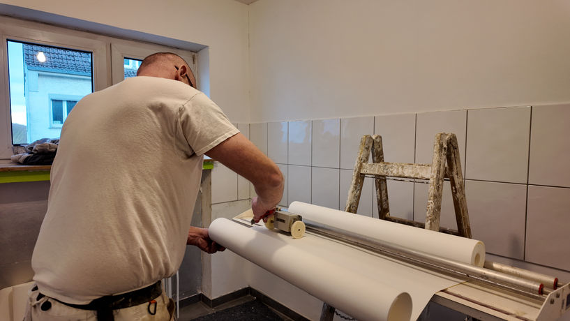 Mitarbeiter von Armin Lindenbeck schneidet ein Stück Tapete ab.