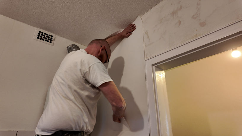 Mitarbeiter von Armin Lindenbeck bringt ein Stück Tapete an die Wand an.