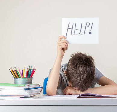 Sad tired frustrated boy sitting at the table with many books and holding paper with word