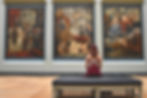 Individual seated quietly in a museum, engaging with framed paintings along the gallery wall.