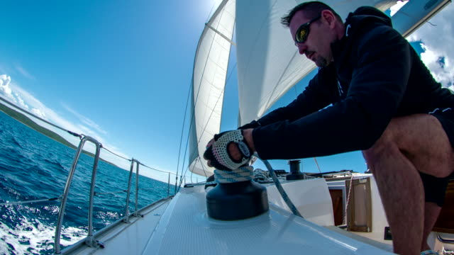 homem enrolando corda em veleiro navegação mar aberto