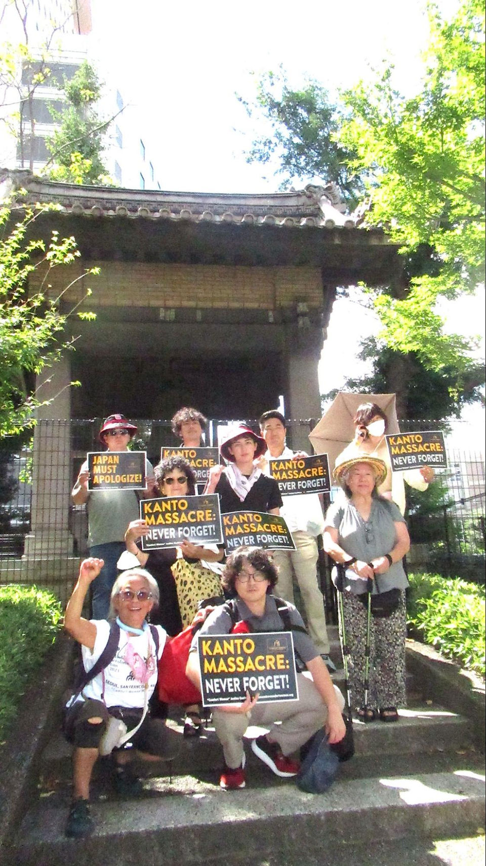 A group of people standing on stairs holding signs raising awareness about the Kanto massacre