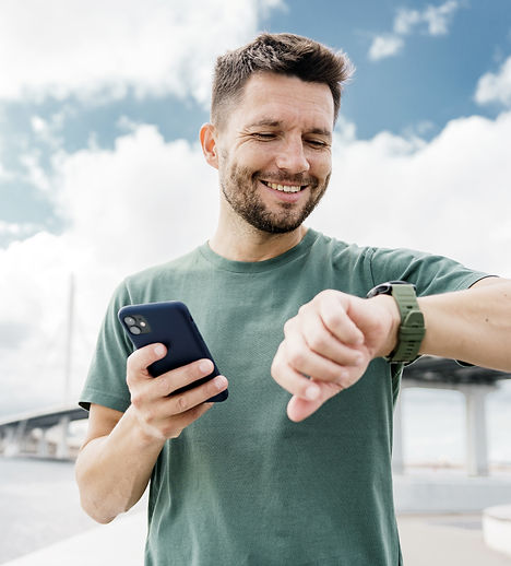 Man smiles, checks watch and phone outside near bridge.jpg
