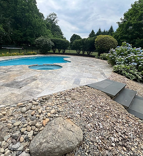 a beautifully landscaped pool renovation with a blue pool, grey tiles, steps, and rocky landscaping