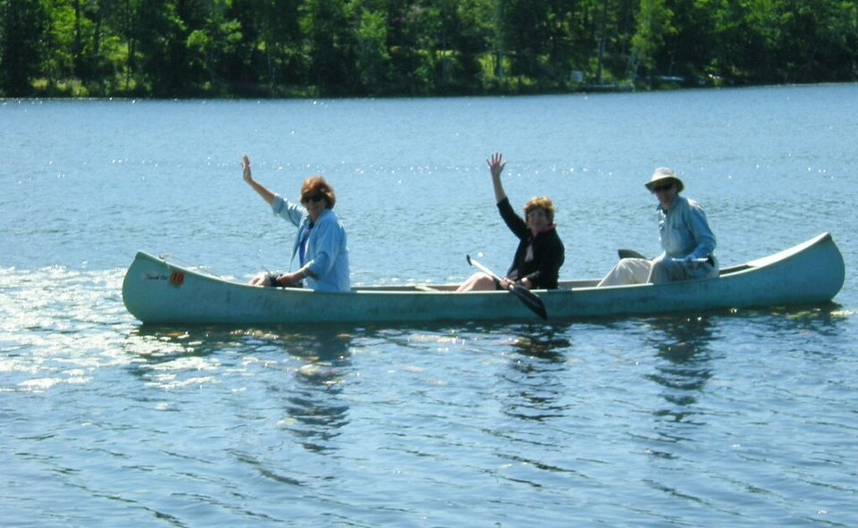 3 women waving from canoe on a lake