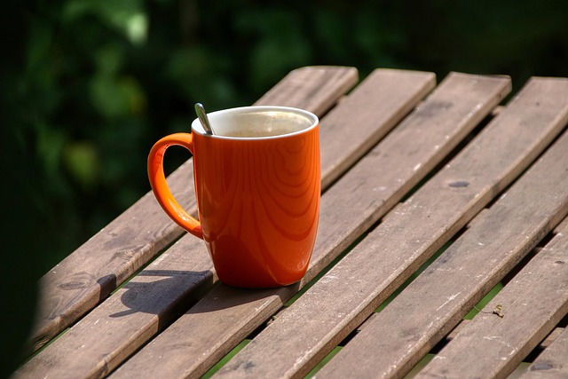 Orange mug of coffee, on an outdoor wooden table.