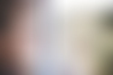 A person sitting by a window in soft light, with their reflection visible in the glass as they look outside thoughtfully.