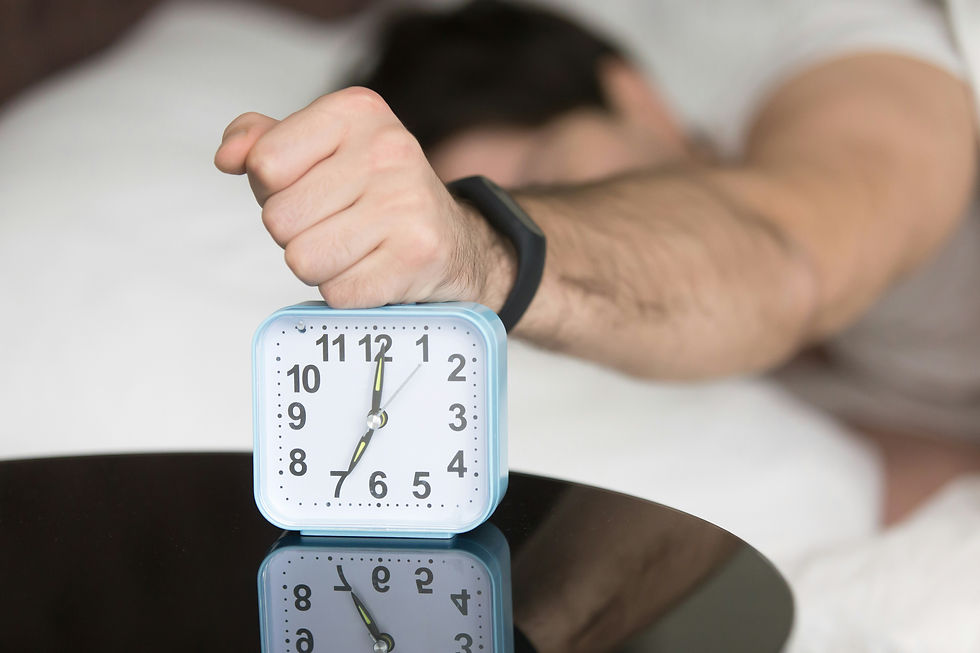 Man lying in bed, stretching is arm out and thumping his fist down on an analogue alarm clock.