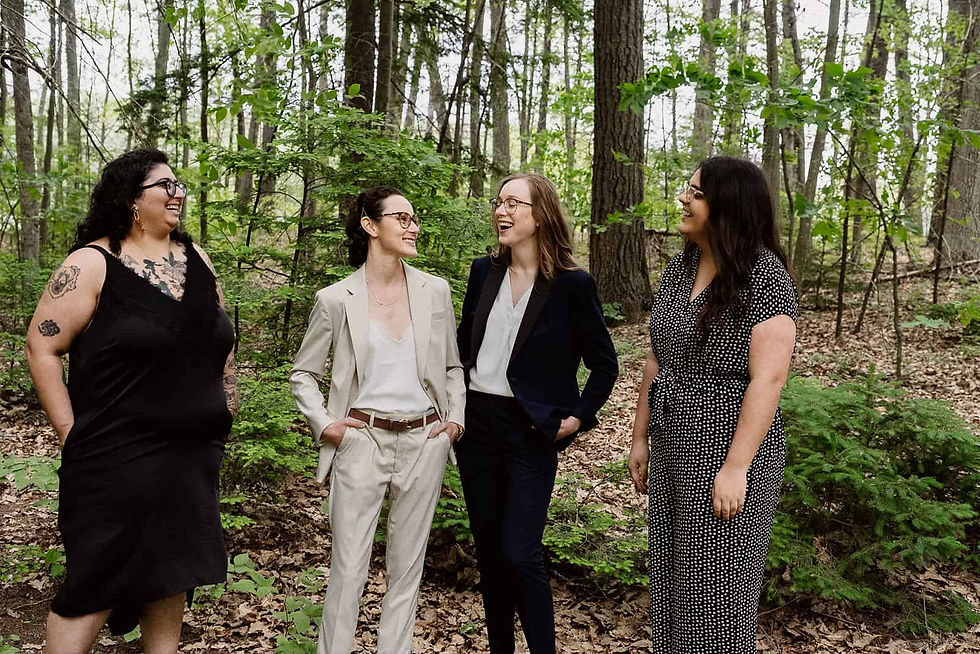 A candid photo of two brides in suits looking at each other laughing. On either side are their two best friends laughing along. LGBTQ Lesbian Elopement Saratoga Springs NY
