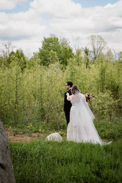 The bride dressed in a white dress stands behind the groom and taps the groom on his shoulder