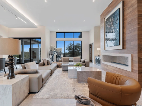 Luxury Interior Design in Texas featuring a modern San Antonio luxury home living room with custom furnishings by Khamila Design House. This Texas Hill Country interior showcases integrated architecture, natural stone fireplace, warm wood paneling, expansive windows, and bespoke seating designed for refined, high-end living.