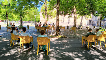 Pause in der Dom-Oase auf dem Domplatz. Die Klasse sitzt auf dem Domplatz auf gelben Stuhlen und macht eine Pause im Schatten der Bäume.