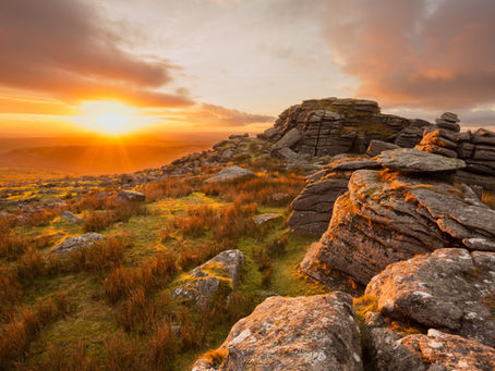 Tramonto rosso fuoco su una formazione rocciosa di granito e un vasto altopiano di brughiera d'erica, con una luce dorata che crea riflessi scntillanti sulle rocce e le nuvole. Atmosfera serana che ispira una sensazione di pace e  tranquillità 