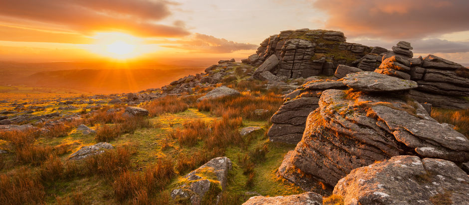 Tramonto rosso fuoco su una formazione rocciosa di granito e un vasto altopiano di brughiera d'erica, con una luce dorata che crea riflessi scntillanti sulle rocce e le nuvole. Atmosfera serana che ispira una sensazione di pace e  tranquillità 