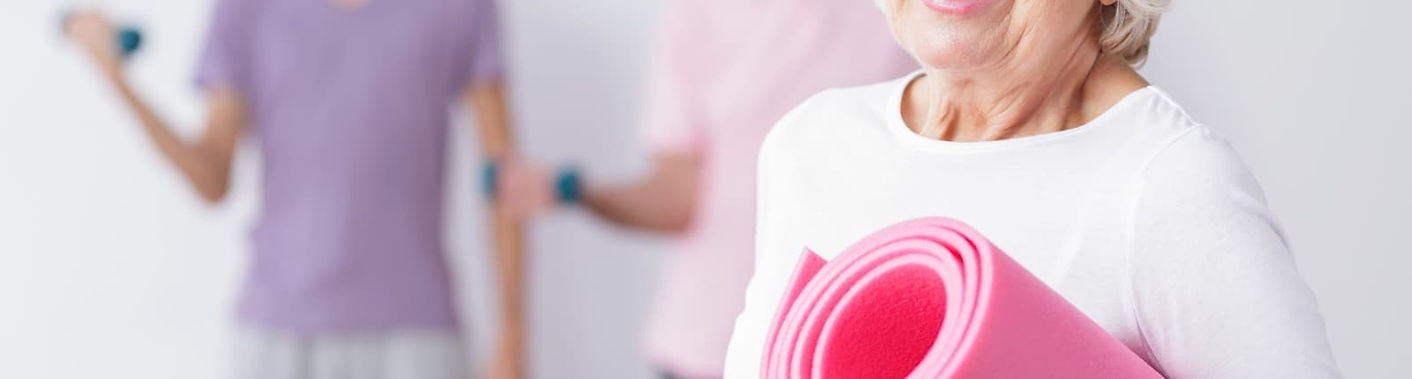 Smiling older woman holding a pink Pilates mat at Redrock Physio in St Albans – promoting Pilates-based physiotherapy for str