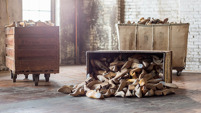 A warehouse room shows bins of shoe making forms. One is overturned and the shoe forms spill on to the floor.