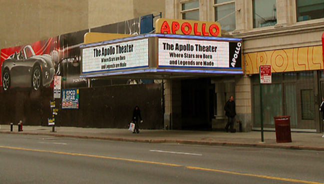 A brick building with a large, lighted sign reading Apollo. A marquee on the front of the building shows coming attractions.