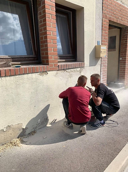 Deux hommes en intervention sur une façade abîmée, préparant un ravalement ou une reprise d’enduit.