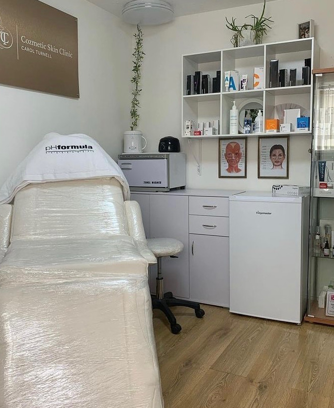 This image shows the treatment room at the clinic, complete with reclining treatment chair and various skin treatment/ care bottles.