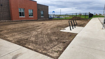 Dirt field with bicycle rack, building at background, cloudy day, empty area.
