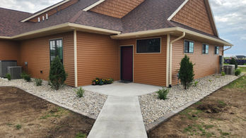 Exterior view of brown building with a concrete walkway and landscaping.