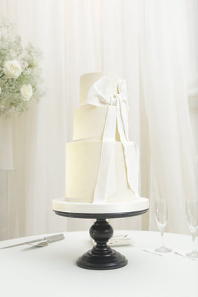 Three-tiered wedding cake with white bow on a black cake stand with white bow at Wimbish House