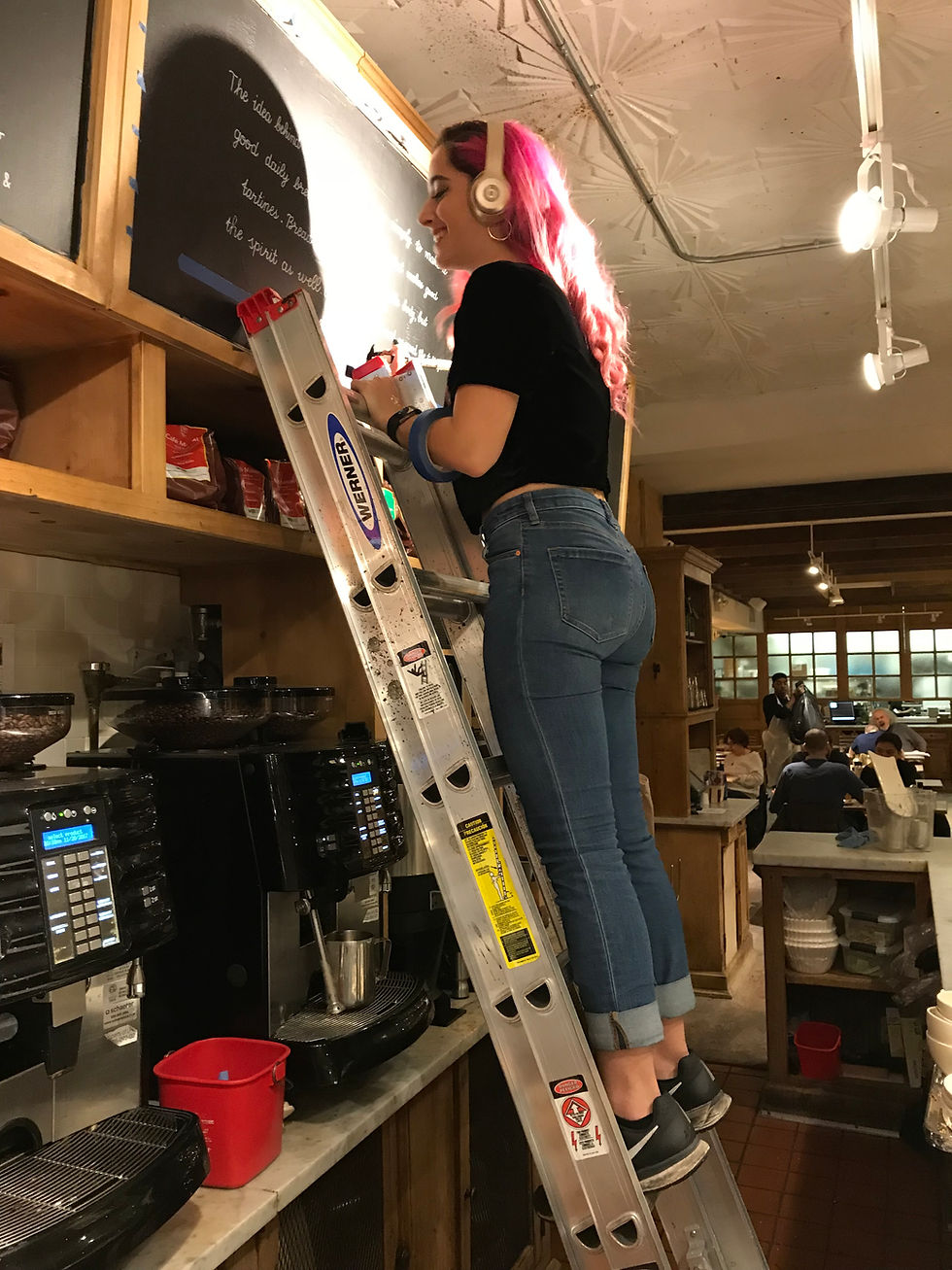 artist on ladder hand writing chalkboard menu and signage for a cafe in New York City