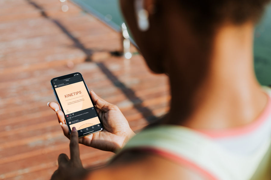 A woman in public wearing athletic clothes. She is on her phone, which is showing an Instagram post. 