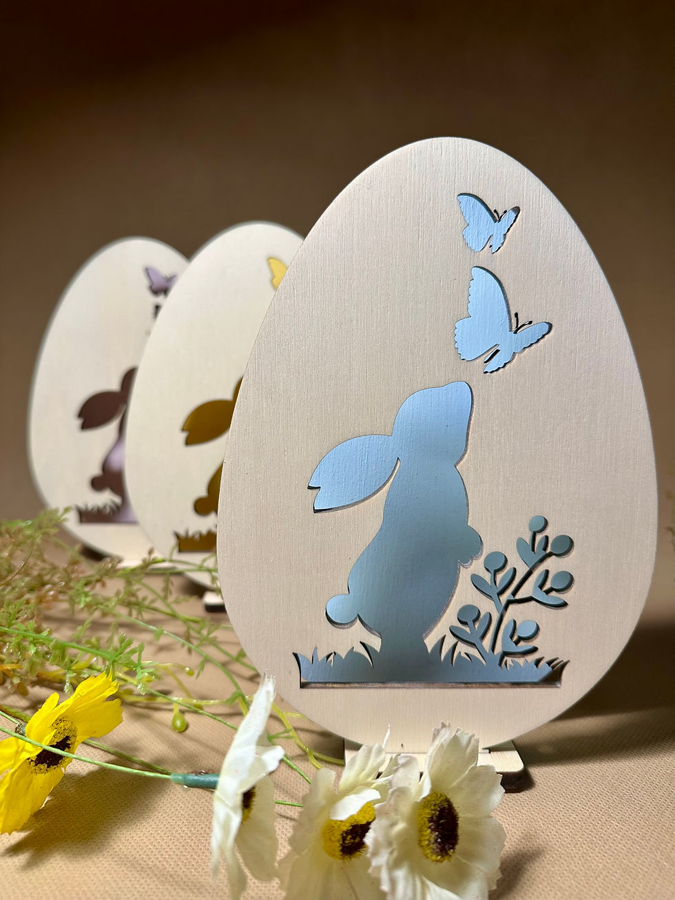 Miniatura: Elegante lampada pasquale in legno a forma di uovo con intaglio di coniglietto e farfalle, illuminata con luce soffusa.