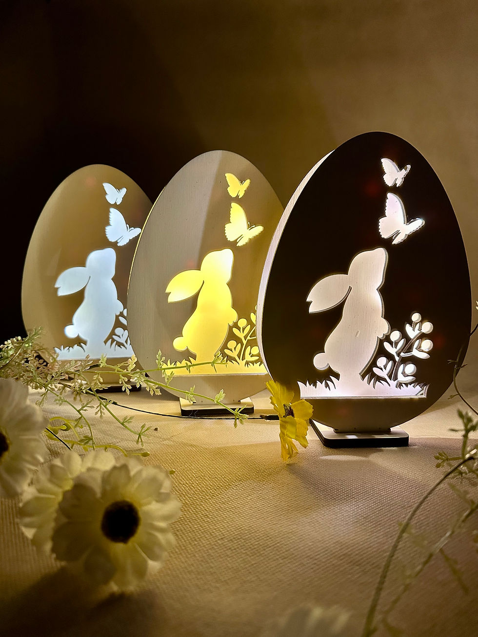 Miniatura: Elegante lampada pasquale in legno a forma di uovo con intaglio di coniglietto e farfalle, illuminata con luce soffusa.