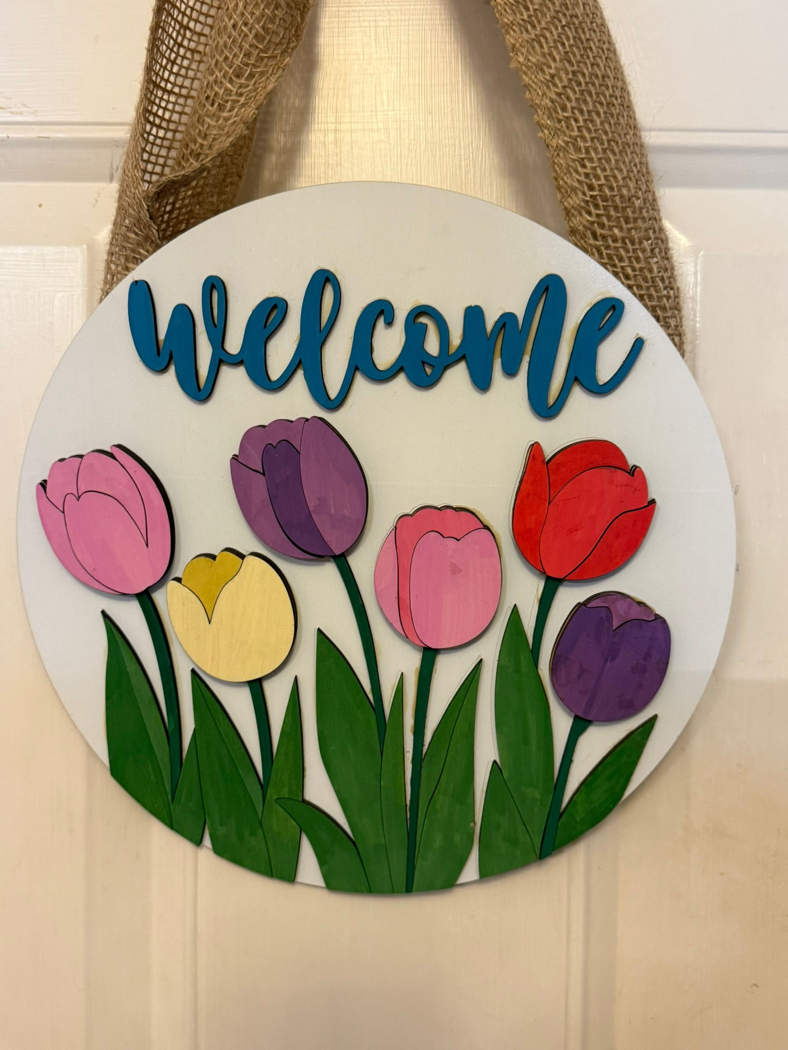 Round welcome sign with colorful tulips hanging by burlap.