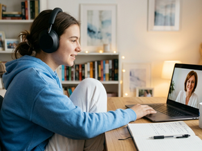 Adolescentă cu căști participând la o ședință de psihoterapie online pe laptop din confortul propriei camere, comunicând cu un psihoterapeut de la Clinica Blue.