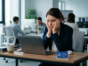 O femeie epuizată (postură de burnout), stă la un birou open-space modern cu capul în mâini. În fața ei este un laptop și o carte de vizită mică, albastră, cu logo-ul Clinica Blue.