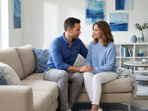 Cuplu înțelegător discutând calm pe o canapea într-un living modern cu decor albastru, ilustrând reconectarea emoțională prin psihoterapie de cuplu la Clinica Blue.